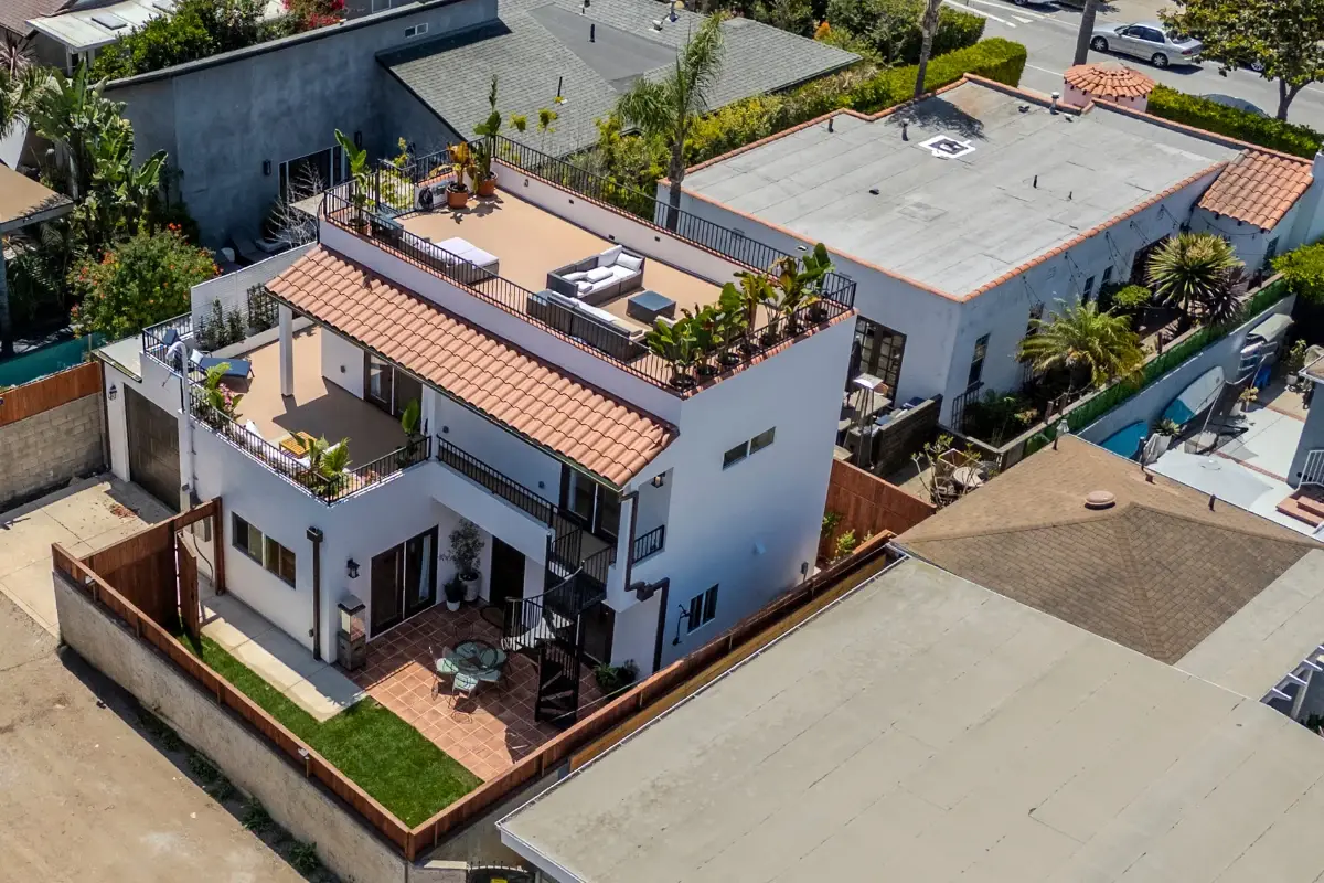 West LA two-story ADU with Mediterranean tile roof and 600 sqft wraparound rooftop deck — aerial view showing outdoor dining and lounge setup