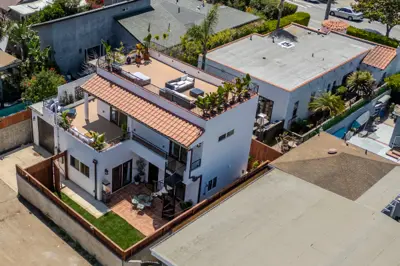 West LA two-story ADU with Mediterranean tile roof and 600 sqft wraparound rooftop deck — aerial view showing outdoor dining and lounge setup