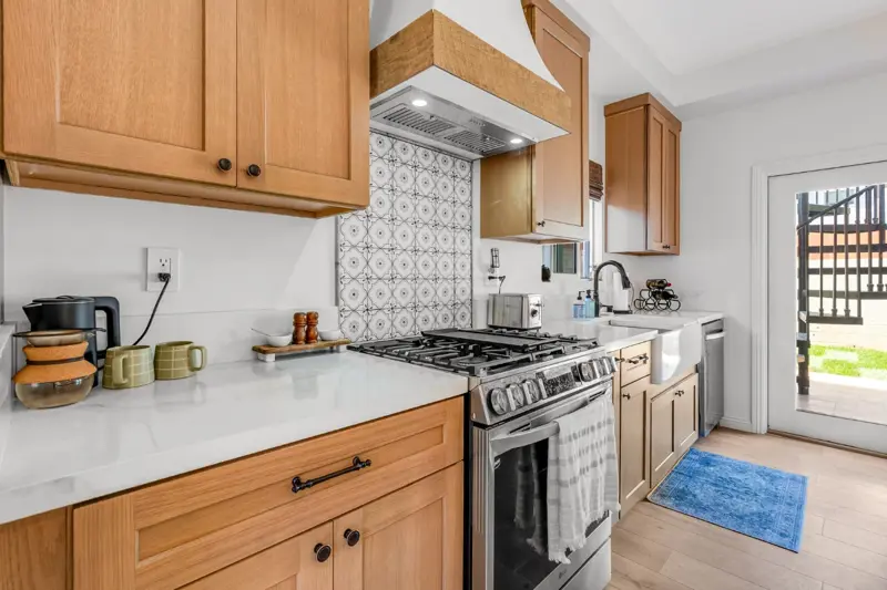 West LA ADU kitchen with solid oak cabinetry, Spanish-tile backsplash, full-size gas range, and white quartz countertops