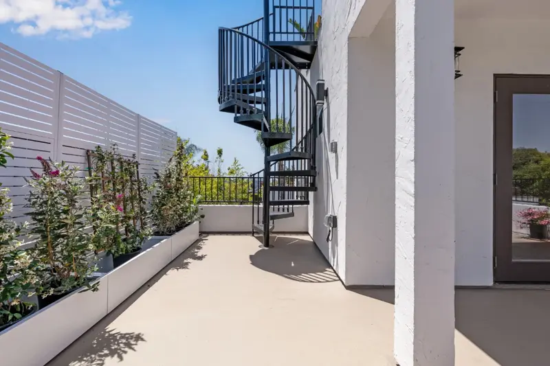 Exterior spiral staircase leading from second-floor deck up to private upper rooftop perch with planters