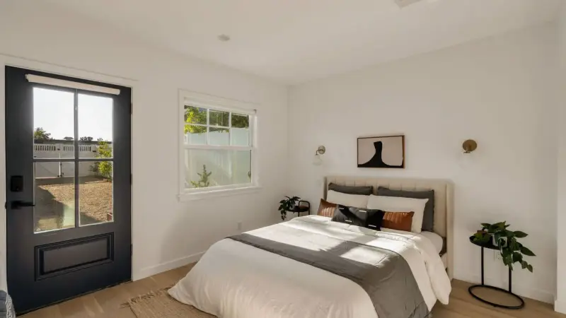 Burbank ADU sleeping area with upholstered headboard, wall sconces, and glass door opening to the private patio