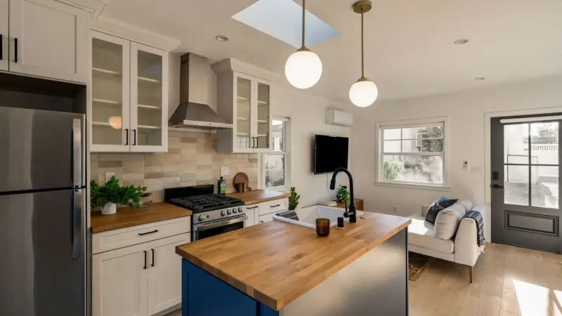Burbank ADU kitchen with navy island, butcher-block countertop, farmhouse sink, matte black faucet, full-size range with chimney hood, and skylights
