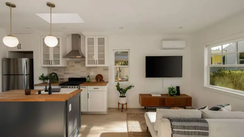 Open-concept kitchen and living area in Burbank studio ADU with white shaker cabinets, butcher-block counters, skylight, and wall-mounted TV