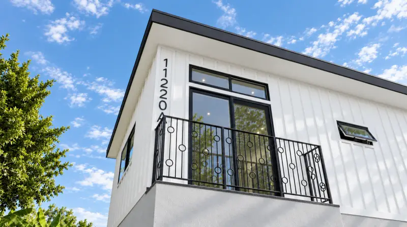 Second-floor balcony of the Culver City ADU with a ring-pattern iron railing, tall black-framed sliding door with transom, and vertical board and batten siding