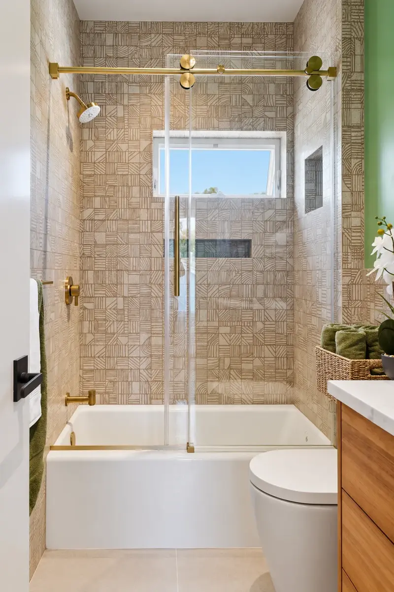 Culver City ADU bathroom with geometric textured tile, brass shower fixtures, a sliding glass door, and a wood vanity
