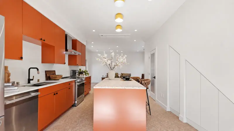 Open-plan kitchen and living area in the Culver City ADU with terracotta cabinets, a long island, and flush white built-in cabinets under the staircase