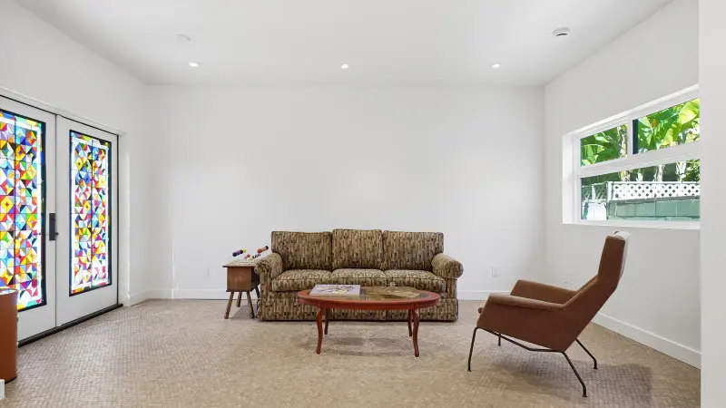 Living room in the Culver City ADU with cork floors, stained glass doors, and a horizontal window framing tropical greenery