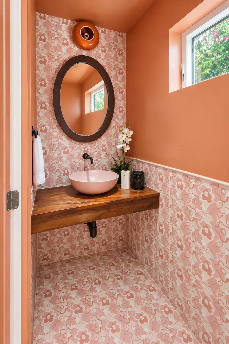 Culver City ADU powder room with pink floral tile on the floor and walls, a wood floating vanity, blush vessel sink, and oval mirror