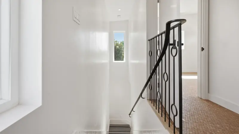 Upstairs landing of the Culver City ADU with a black iron railing in a ring pattern, a tall narrow window, and cork floors