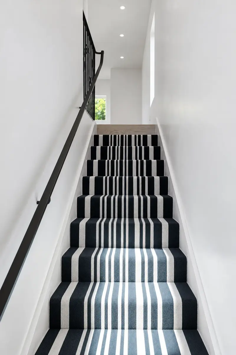 Staircase in the Culver City ADU with a navy and white striped runner, black handrail, and a window at the top of the stairs