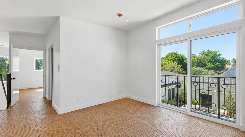 Upstairs room in the Culver City ADU with cork floors and a tall sliding door with transom window overlooking the shared courtyard