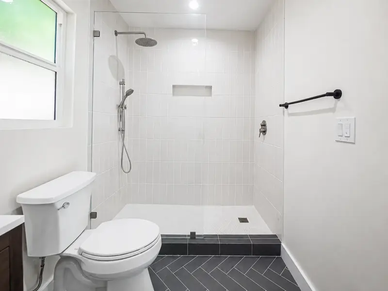 Frameless glass walk-in shower with stacked vertical white tile, full-width niche, and rain head in the Mar Vista ADU