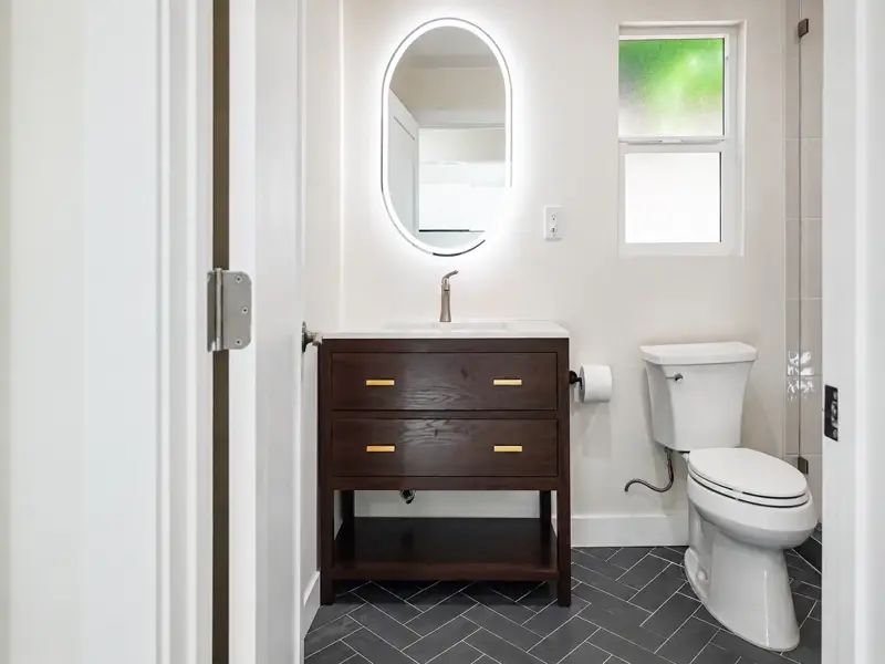 Walnut vanity with brass pulls and a backlit oval mirror in the Mar Vista garage conversion ADU bathroom