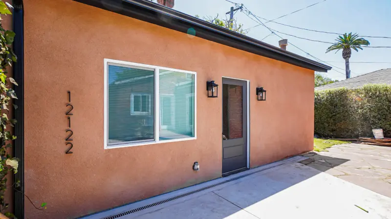 Entry of the Mar Vista garage conversion ADU — obscure-glass door, paired black lanterns, and oversized black address numbers on terracotta stucco
