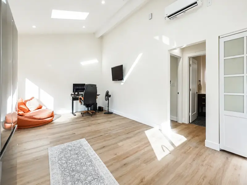 Living area of the Mar Vista ADU with vaulted ceiling, skylight, ductless mini-split, and a frosted-glass door to the bathroom