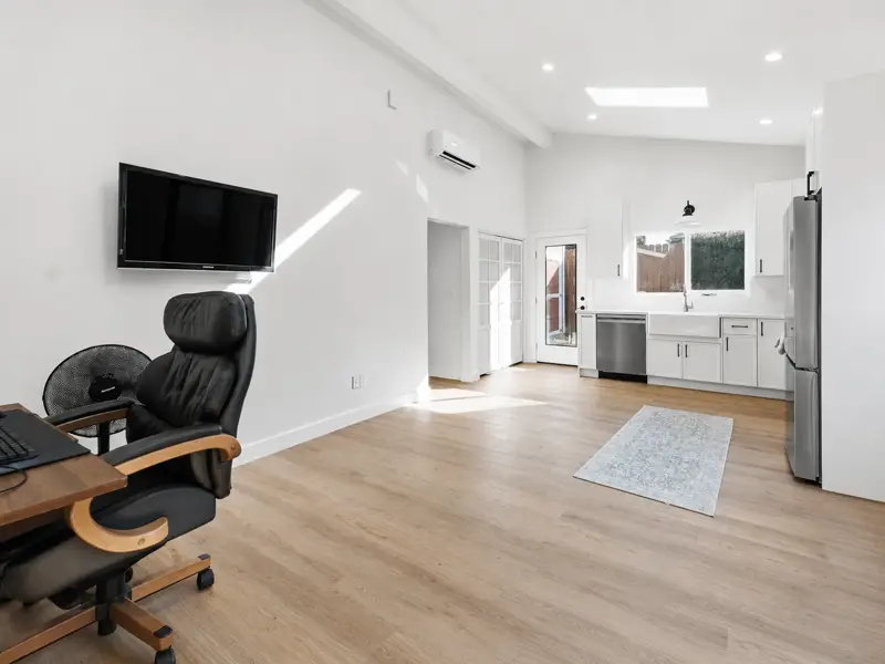 Open living area and kitchen in the Mar Vista ADU under vaulted ceilings with an exposed beam, skylights, and wide-plank wood-look flooring