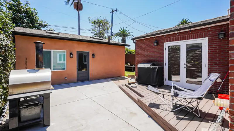 Shared concrete patio between the Mar Vista ADU and the red-brick main house, with a deck and outdoor pizza oven