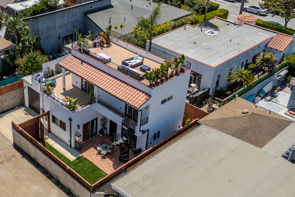 West LA two-story ADU with Mediterranean tile roof and 600 sqft wraparound rooftop deck — aerial view showing outdoor dining and lounge setup