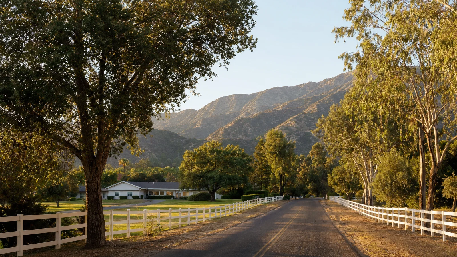 Building an ADU in Bradbury, CA — a rural estate lane with white rail fencing, mature oaks and the San Gabriel Mountain foothills behind, where CALI ADU designs and permits single-story Signature Home ADUs under Bradbury Development Code Chapter 85