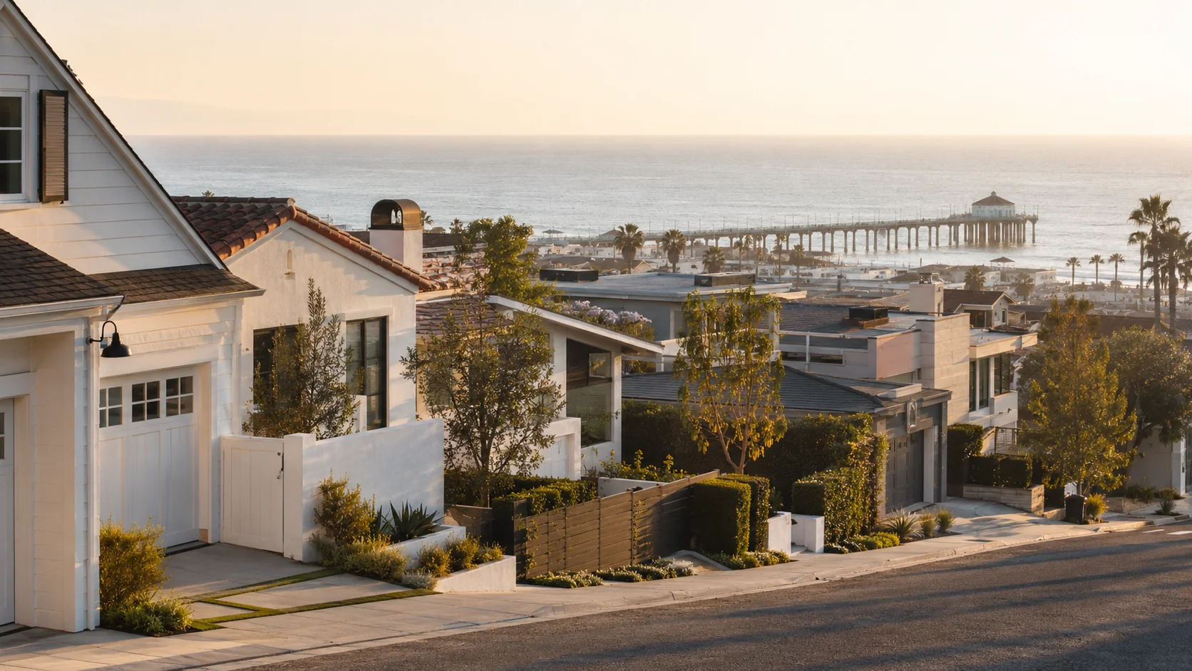 Coastal residential street descending toward the Pacific in Manhattan Beach with modern white coastal homes and the Manhattan Beach Pier visible at the horizon at golden hour