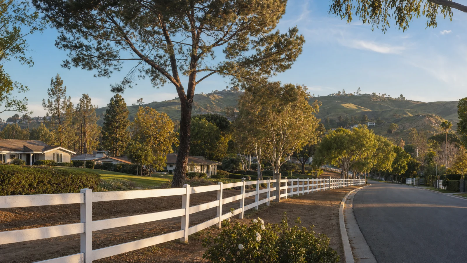 Building an ADU in Rolling Hills Estates, CA — white three-rail ranch fencing along a dirt bridle trail beside a residential street, with single-story ranch homes on large lots and the rolling Palos Verdes hills behind, where CALI ADU designs and permits backyard ADUs under RHEMC Chapter 17.56.