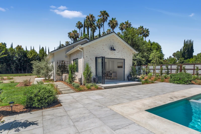 Traditional white stucco gable pool house ADU with French doors and pool in the foreground