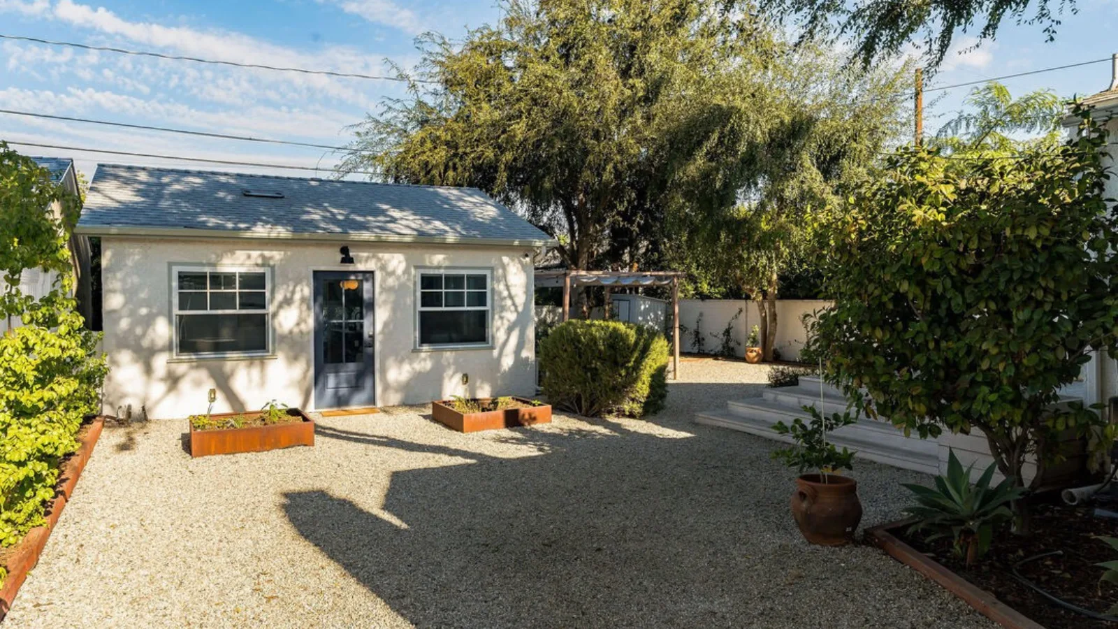 Burbank garage conversion ADU — white stucco exterior with dark-framed glass entry door, skylight, and drought-tolerant landscaping with corten planters